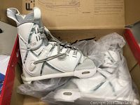 Pair of white and grey wakeboard bindings with laces and padded ankle support inside the original box with plastic coverings.