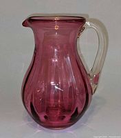 Side view of cranberry glass pitcher showing shape, color and clear handle