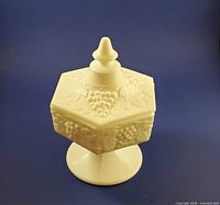 Front view of covered white milk glass hexagon compote showing grape and leaf relief and pedestal base