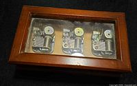 Top view of wood music box showing three visible metal movements under glass
