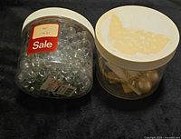 Both plastic canisters side by side, lids visible, contents visible (glass marbles; tiebacks)