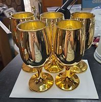 Group of five matching gold-tone goblets standing upright