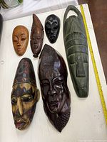Front view of six carved wooden masks showing designs and finishes