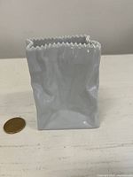 Front view of white porcelain crinkled paper bag vase beside coin for scale