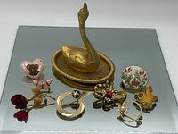 Overview of swan ring holder and eight brooches on mirrored surface