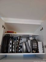 Cabinet shelf showing entire assortment of stacked pans, bundt pan and ramekins