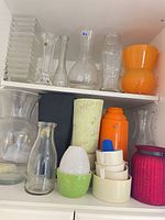 Cabinet shelf showing assortment of vases, thermos, planters and candle holder