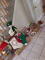 Group view by staircase showing plush snowman, stockings, Santa hat, cardboard box and baskets