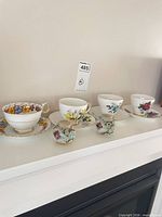 Four teacup and saucer sets displayed with three round floral shakers; lot tag visible