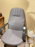 Front view of gray fabric office chair beside small lamp and dresser
