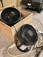 Two Honeywell desk fans inside and beside wood crate with power strip cords visible