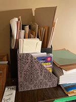 Front view showing gray cardboard file holder with scroll design containing sealed iSlice opener and assorted envelopes, adjacent stacks of paper