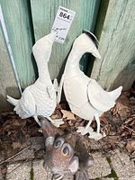 Pair of white metal ducks and brown frog ornament at fence corner, overall view