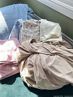 Stack showing blue throw, pink towel, beige fitted sheet, floral flat sheet, pillowcase