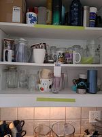 Cabinet shelves filled with assorted mugs, glasses, travel mugs, pitcher, stein