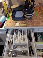 Dinner plates, bowls, mugs stacked on countertop with flatware tray beneath