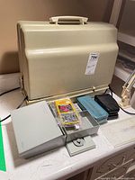 Closed hard case with accessory boxes, needle pack, foot pedal visible