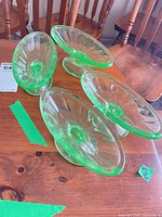 Four green uranium glass footed bowls on wooden table