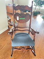 Front view of rocking chair showing carved crest, slat back and upholstered seat