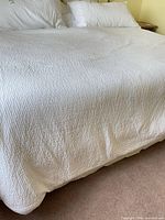 Full view of white textured coverlet on bed with shams