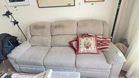 Front view of beige three-seat reclining sofa with pillows