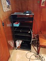 Front view of black media cabinet with glass door closed, showing shelves and casters