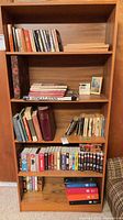 Full bookshelf showing paperbacks, VHS tapes, binders, framed print and bookcase