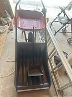 Front view showing snow scoop with hand shovel resting inside and wheelbarrow behind