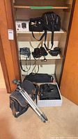 Entire lot showing camcorders, SLR camera, lenses, flash, tripod, bags and cables arranged on closet shelves