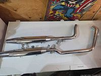 Two chrome Harley-Davidson mufflers, one with curved pipe, overall view