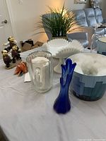 Group shot showing milk glass compote, blue bud vase, clear pitcher, blue vessel, figurine and artificial plant