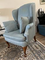 Front angled view of armchair showing upholstery, one pillow and wood legs