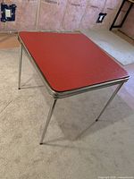 Full view of red square table top with chrome edge and legs