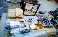 Overview of lot on table showing framed textile art, fabrics, tools and trays