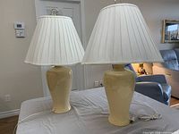 Two beige ceramic table lamps with pleated shades on tabletop
