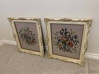 Both framed needlepoint pictures leaning against wall