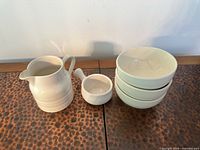 All five cream earthenware pieces: pitcher, handled pot, three stacked bowls