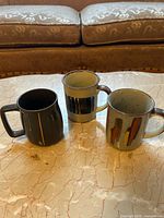 Front view of three ceramic mugs displaying designs