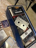 Blue box filled with multiple Maxell cassette tapes, additional cases laid out