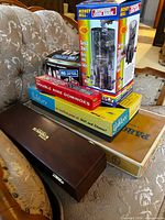 Stacked lot showing all boxed games, dominoes, Rummikub case and Money Mill bank