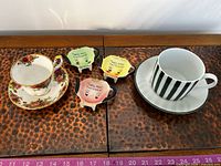 Royal Albert teacup & saucer left, striped cup & saucer right, three teabag holders centre