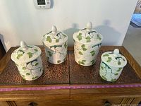 Front view of all four ceramic canisters with lids aligned on surface