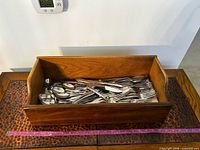 Wood tray filled with assorted stainless flatware, ruler for scale