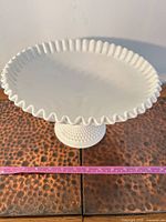 Oblique view showing entire cake stand, ruffled rim, pedestal, tape for scale