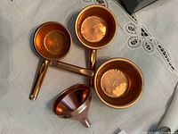 Top view of three copper measuring cups and funnel showing interior finish and stamped markings