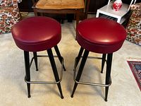 Two red vinyl bar stools front view showing seats, legs, and footrests