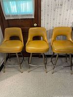 Front view of three mustard vinyl counter stools showing upholstery, legs, and footrests
