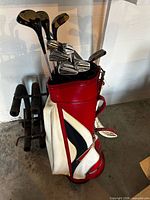 Full view of red and white golf bag loaded with clubs on stand
