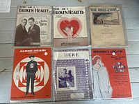 Six assorted vintage sheet music pieces laid out showing illustrated covers