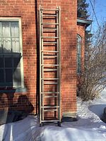 full view of ladder leaned against brick wall in snow